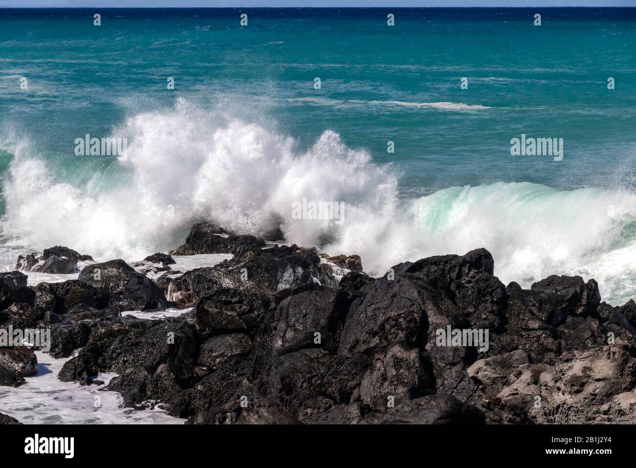 Weiße Welle, die gegen schwarze vulkanische Felsen an der Kona-Küste von Hawaii Big Island bricht. Lebendiger blaugrüner pazifischer Ozean in der Ferne. Stockfoto