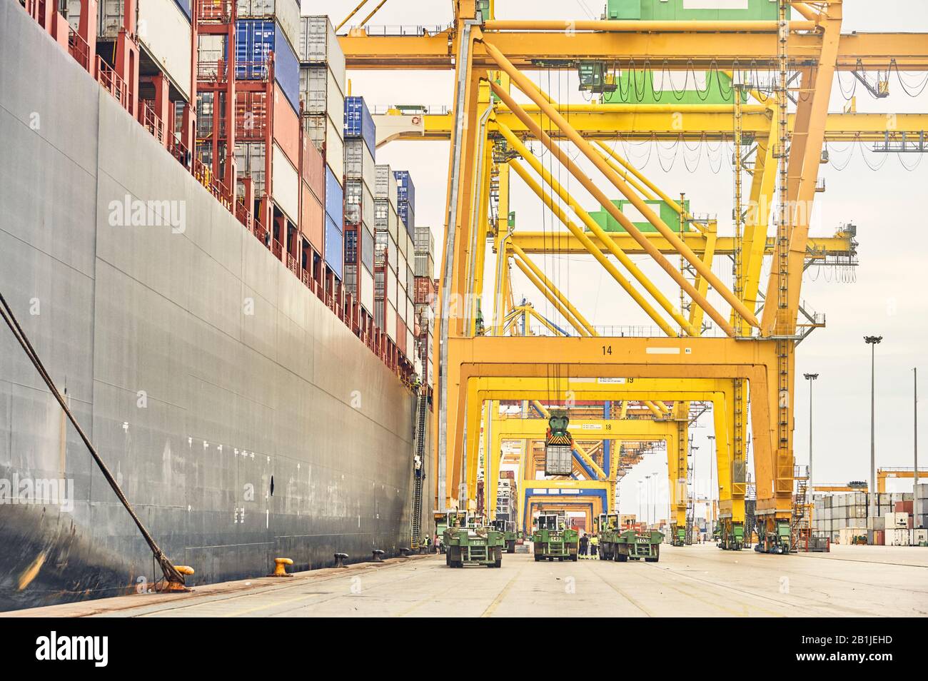 Schiff-Ufer-Kranbeladung Container-LKWs von Frachter entlang der Hafendocke. Infrastruktur für den Seeverkehr und Versandlogistik. Exportieren Sie ein Stockfoto