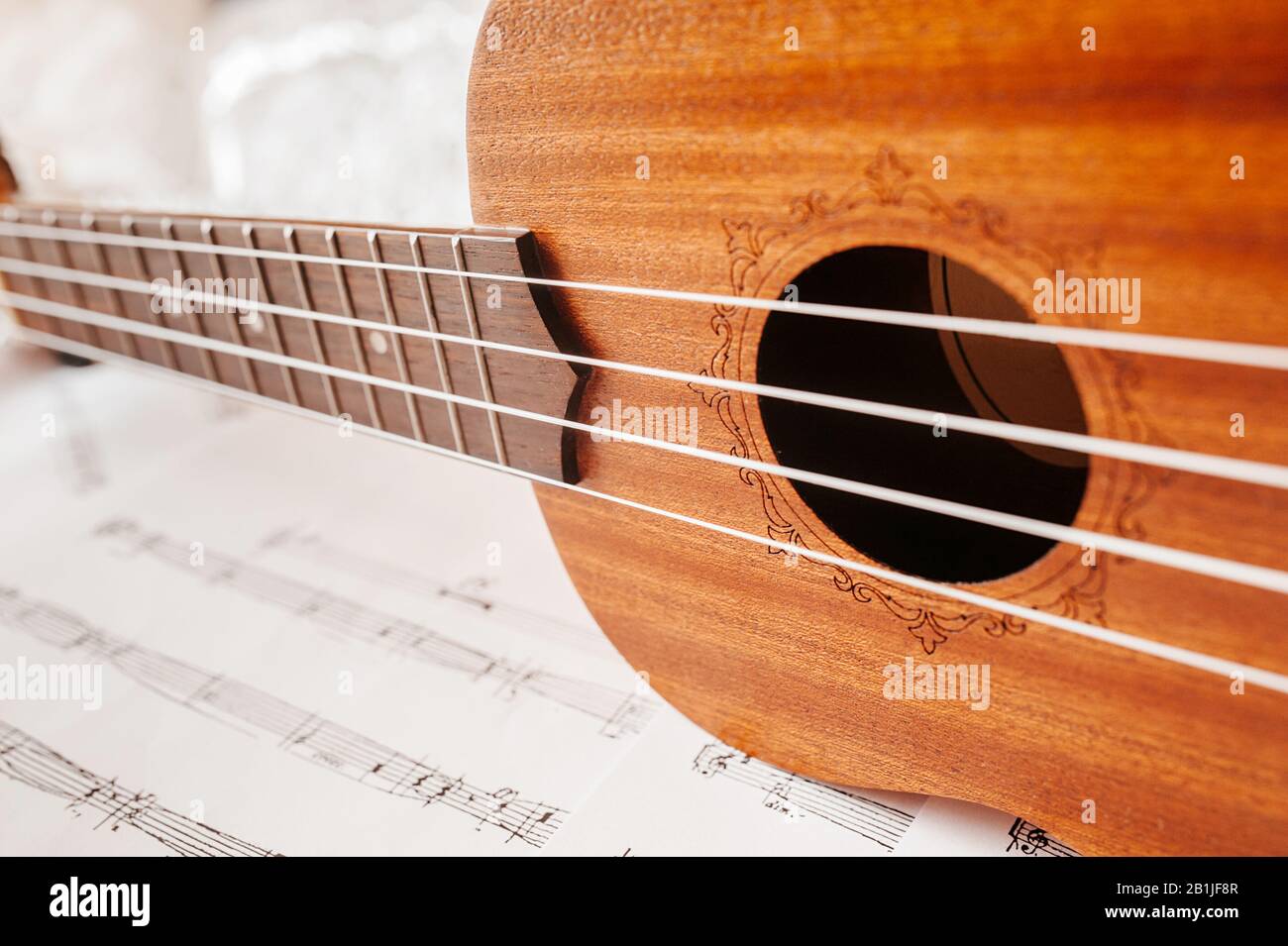Der Hals einer traditionellen Ukulele-Gitarre. Ukulele mit weißen Nylonsaiten auf dem Hintergrund musikalischer Noten. Lifestyle, Stimmungslage. Stockfoto