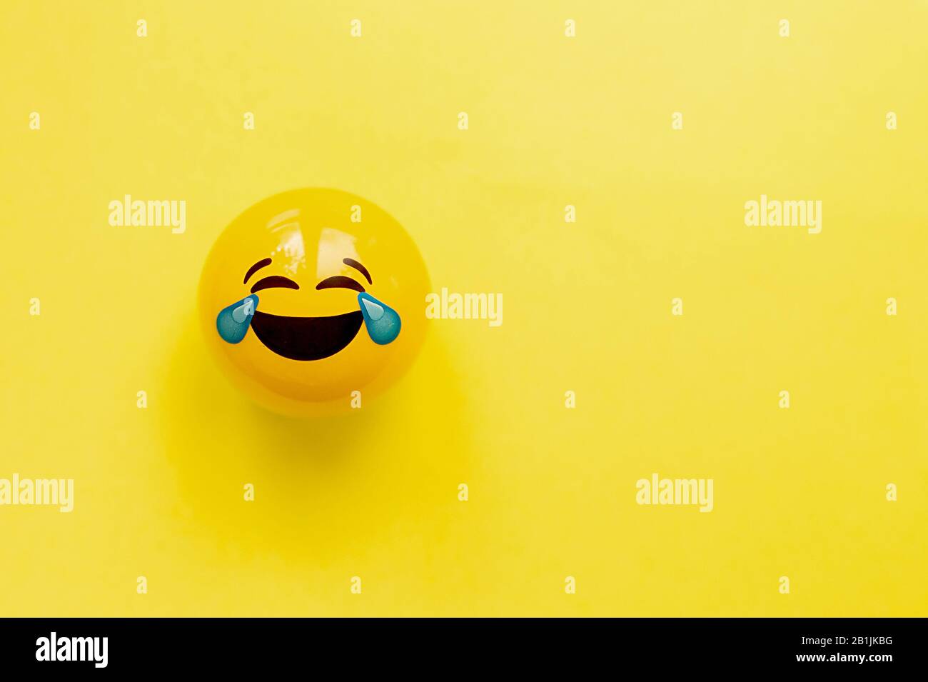 Komisch gelbes Gesicht lacht sehr viel zu Tränen auf einem gelben flachen Hintergrund. Flaches Layout, Draufsicht, Mockup Stockfoto