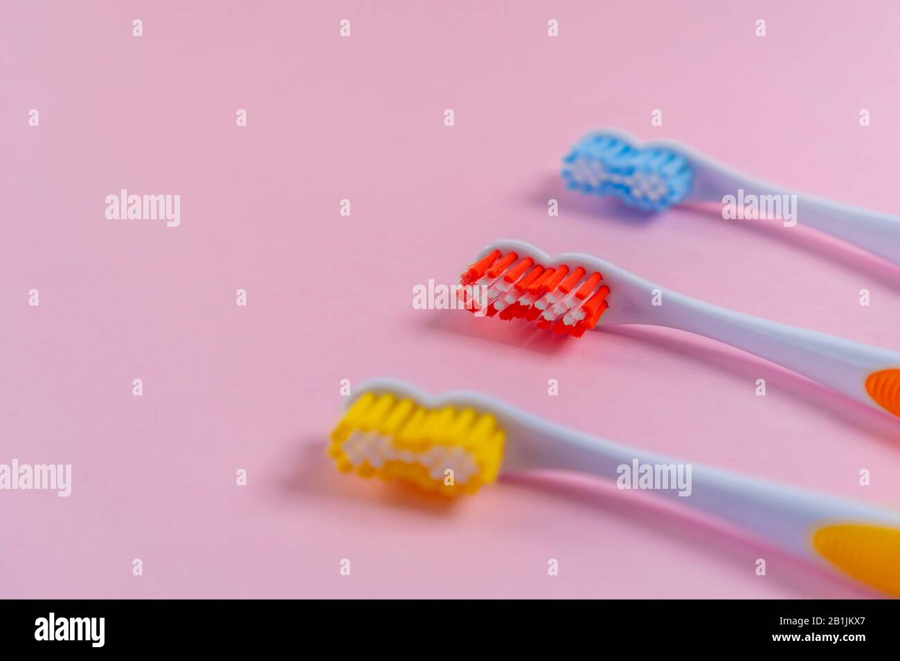 Drei helle Zahnbürsten auf einem zarten rosafarbenen Hintergrund. Rot, Gelb, Blau. Familienbeziehungskonzept Stockfoto