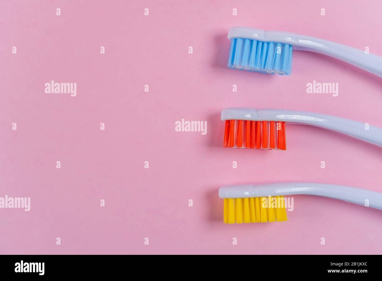Drei farbige Zahnbürsten auf pinkfarbenem Hintergrund. Rot, Gelb, Blau. Copyspace. Helles Werkzeug für Zahnhygiene Stockfoto