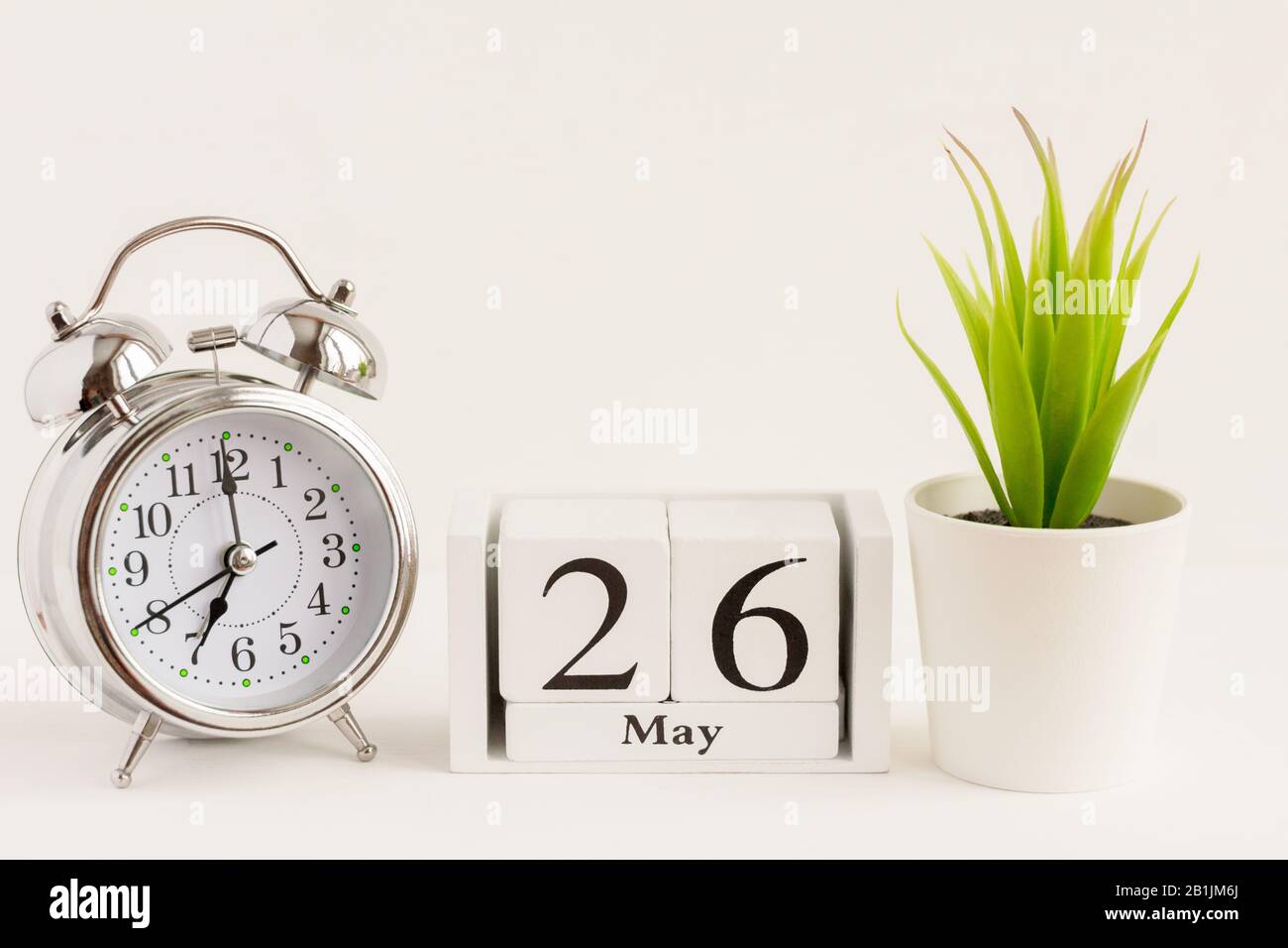 26. Mai auf einem Holzkalender neben einem Wecker und einer Blume. Ein Tag des Frühlingsmonats, Kalender und Wecker auf hellem Hintergrund. Frühling i Stockfoto