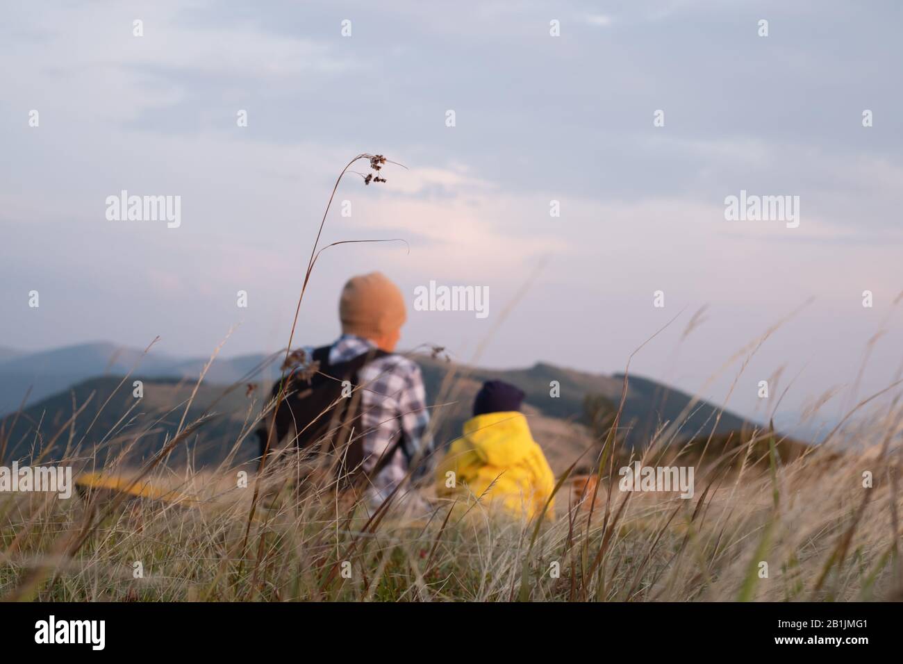 Papa mit Sohn in den Frühlingsbergen in hohem Gras sitzen. Familiencamping. Reisen mit Kinderkonzept Stockfoto