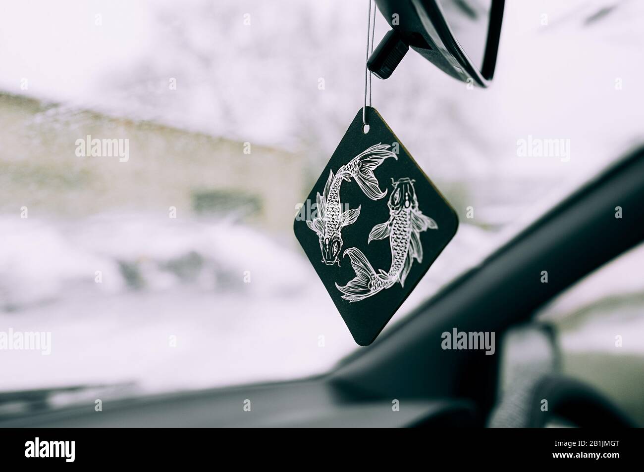 Frischer im Auto in Form einer Zeichnung des Tierkreiszeichens eines Fisches auf einem schwarzen Quadrat auf dem Hintergrund einer schneebedeckten Windschutzscheibe. Stockfoto