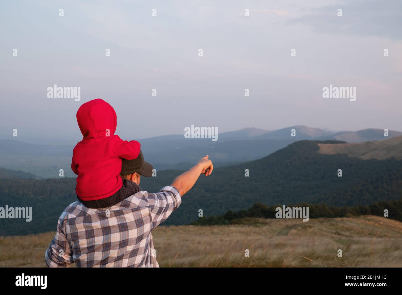 Papa mit Sohn in den Frühlingsbergen in hohem Gras sitzen. Familiencamping. Reisen mit Kinderkonzept Stockfoto