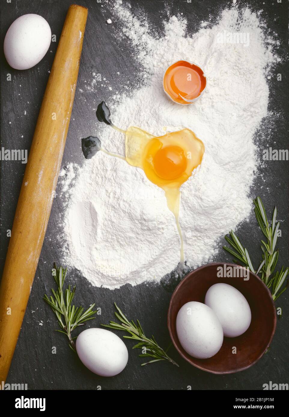 Backkäse Plätzchen Rezeptfoto leerer Essenshintergrund mit Rollstift zerbrochene Eier, Mehl und Rosmarin auf Schiefersteinoberfläche. Platz für te kopieren Stockfoto