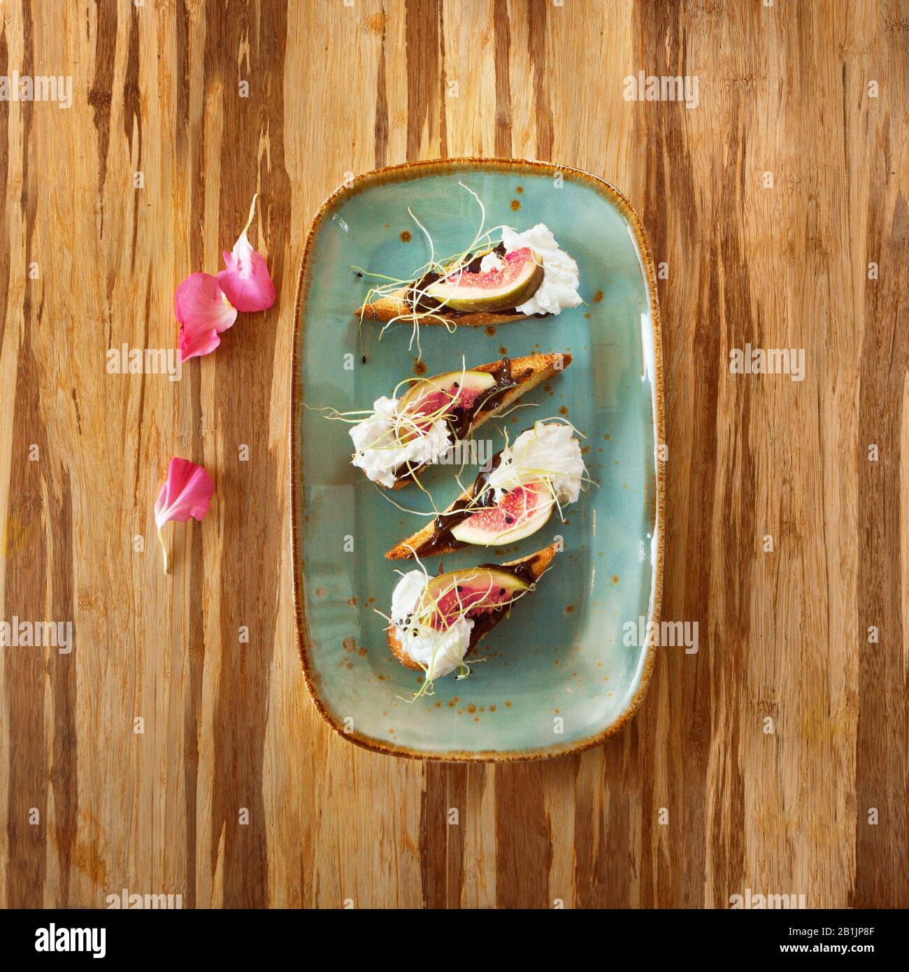 Marokkanisches Dessertgericht mit Creme, Schokolade und Feige auf einem Teller, mit Blumenblättern dekoriert, auf einem Holztisch und Platz für Text Stockfoto