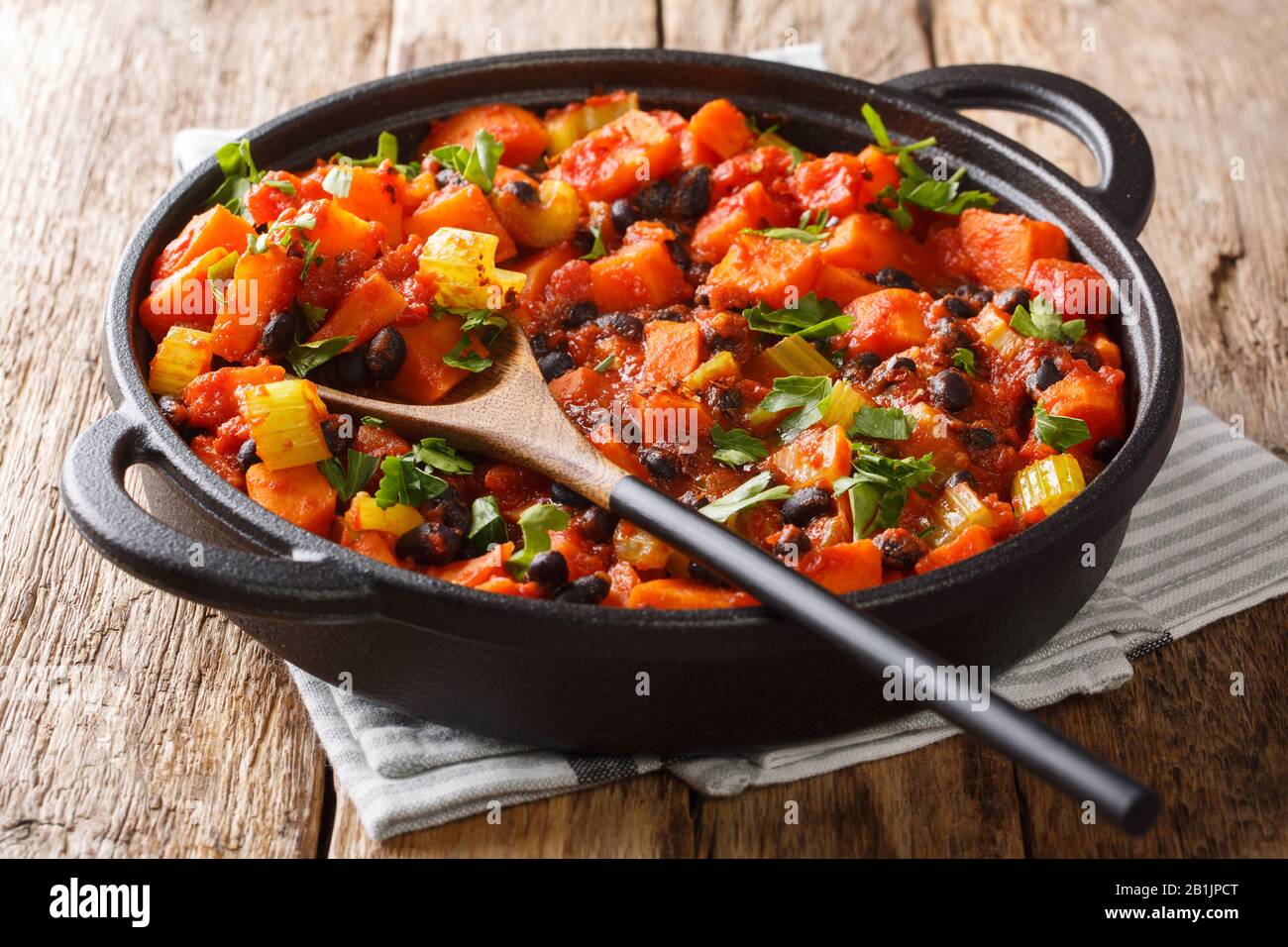 Traditionelles Rezept für Chili Süßkartoffeln und schwarze Bohnen mit Tomaten, Sellerie in einer Pfanne auf dem Tisch. Horizontal Stockfoto