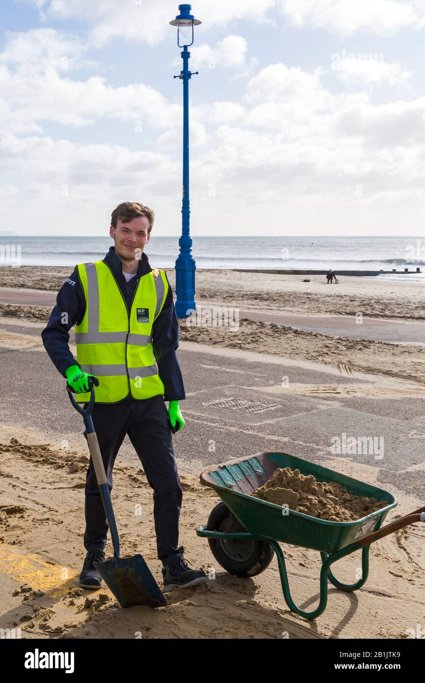 Bournemouth, Dorset, Großbritannien. Februar 2020. Stadtrat Lewis Allison bleibt stecken und gibt den Rangern am Meer eine Hand, um den Sand von der Promenade zu entfernen, der von den jüngsten starken Winden und dem Sturm Dennis geblasen wurde. Stadtrat Allison ist Labour-Ratsherr für Boscombe West und Portfolio-Inhaber, Kabinettsmitglied, für Tourismus, Freizeit und Gemeinden im BCP-Rat (Bournemouth, Christchurch und Poole). Credit: Carolyn Jenkins/Alamy Live News Stockfoto