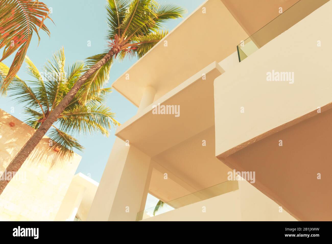 Abstrakter architektonischer Hintergrund mit weißer Außenfläche und Palmen unter blauem bewölktem Himmel, stilisiertes Foto mit Vintage-Farbkorrekturfilter Stockfoto