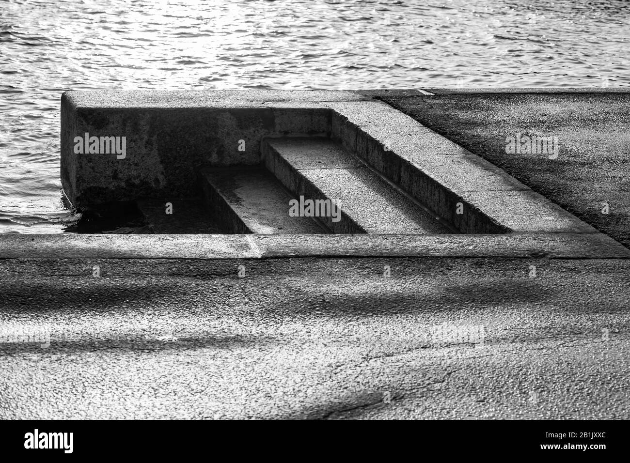 Dunkle, nasse Treppen aus Granit gehen hinunter zum Flusswasser. Schwarz-weiß abstrakter Fotohintergrund für Architekturfotos. St. Petersburg, Russland Stockfoto