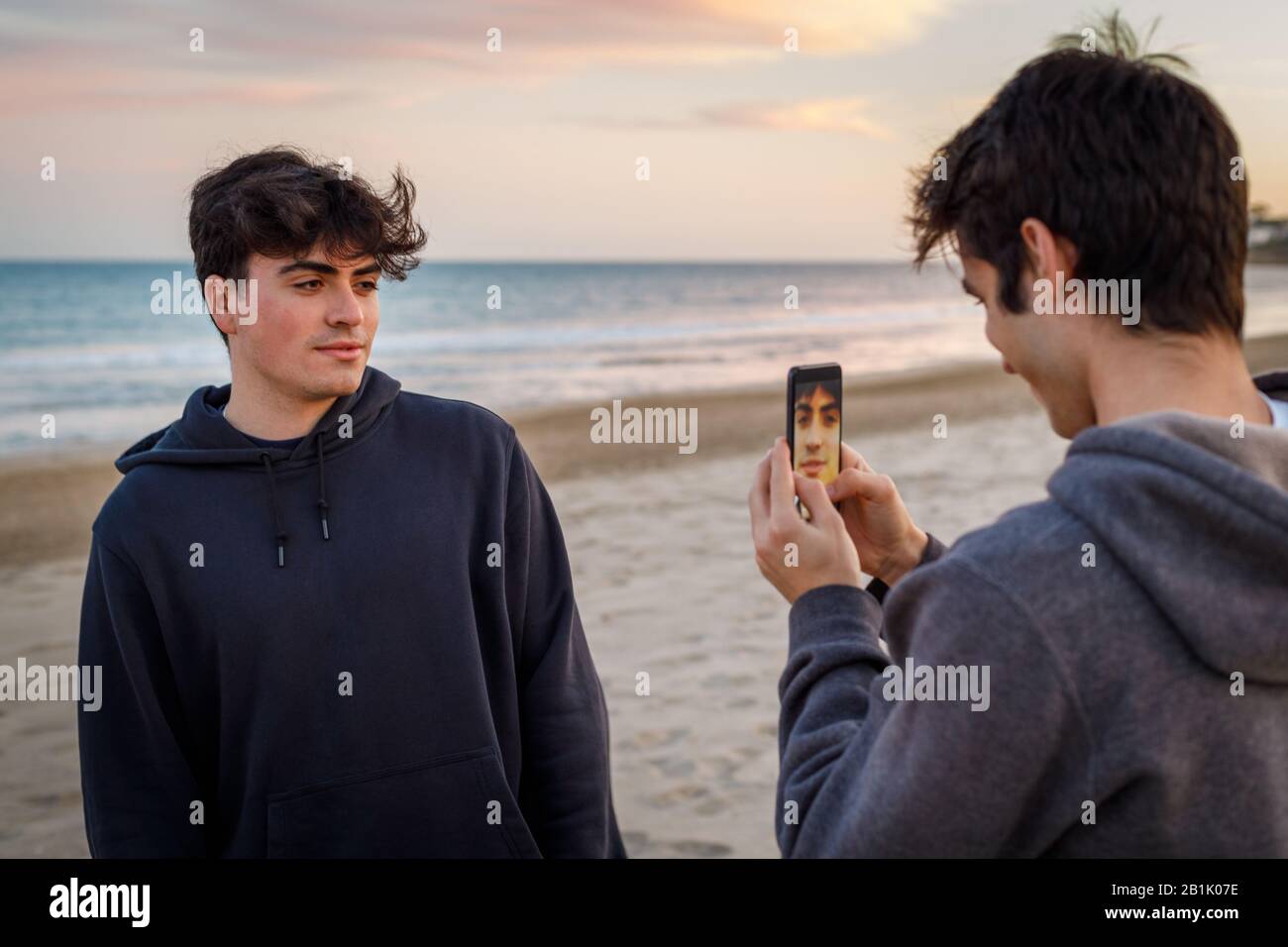 College-Junge, der bei Sonnenuntergang ein Handy-Foto eines Freundes am Strand aufgenommen hat Stockfoto