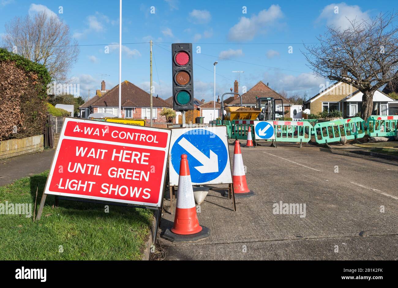 "Warten Sie hier, bis grünes Licht aufleuchtet" Warnschild an einer 4-Wege-Kreuzung an Straßenbaustellen, mit vorübergehender Ampel in England, Großbritannien. Stockfoto
