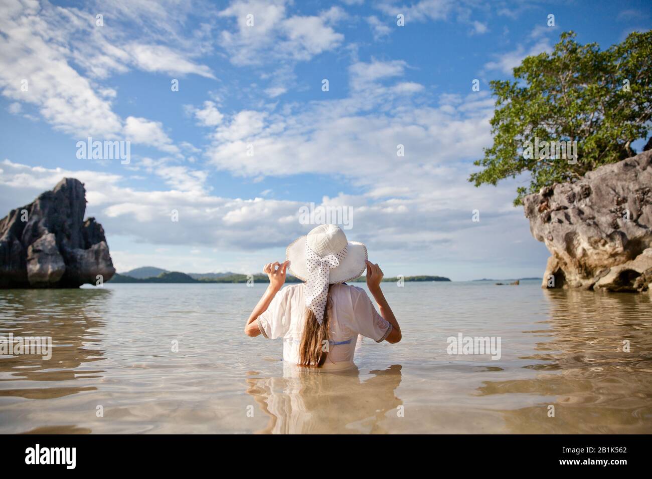 Ein junges Mädchen in einem weißen Hut sitzt im Wasser auf einer tropischen Insel und genießt einen Urlaub. Sommer- und Urlaubskonzept Stockfoto