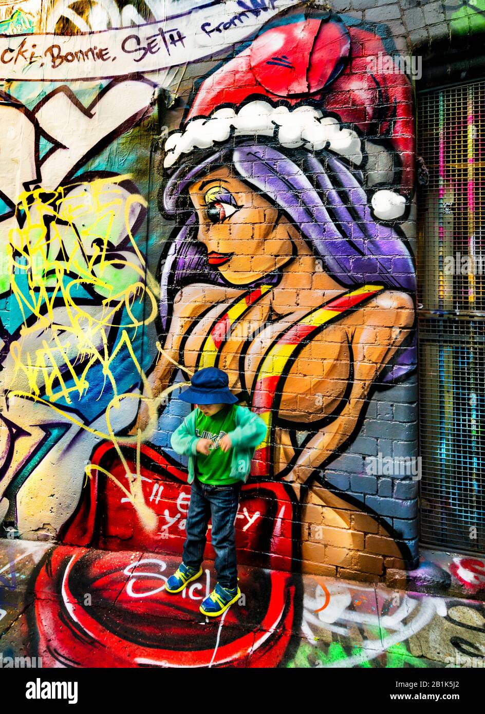 Großes Graffiti-Gemälde im Cartoon-Stil einer Frau mit Weihnachtshut und jungen Jungen, die auf der Straße stehen, Hosier Street, Melbourne Lanes, Melbourne, Vic Stockfoto