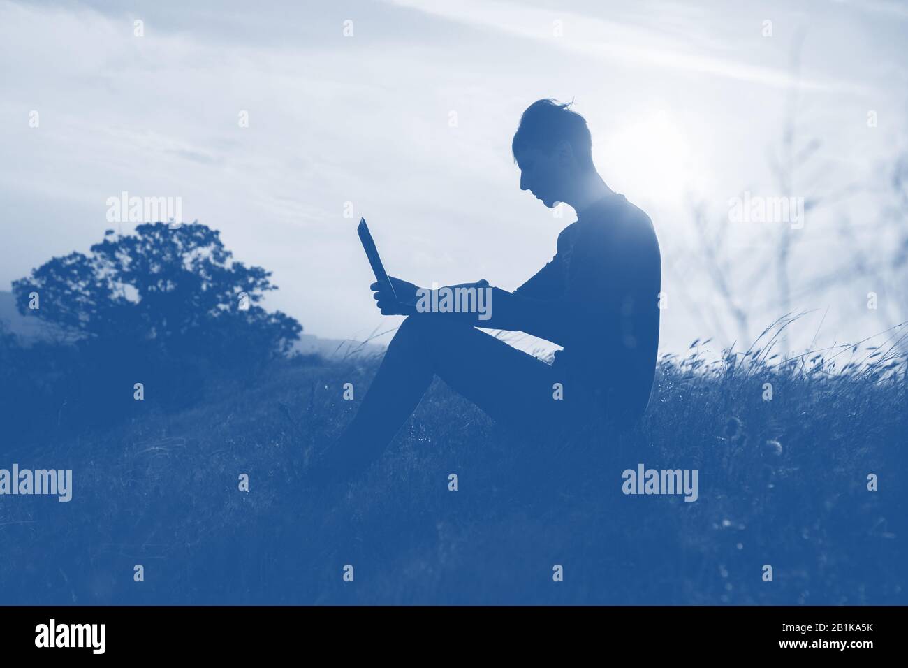 Silhouette eines Mannes gegen den schönen romantischen Himmel bei Sonnenuntergang mit Wolken. Ein Mann arbeitet auf einem Laptop in der Natur, dringendes Geschäft. Trendy Classic Blue 2020 Co Stockfoto