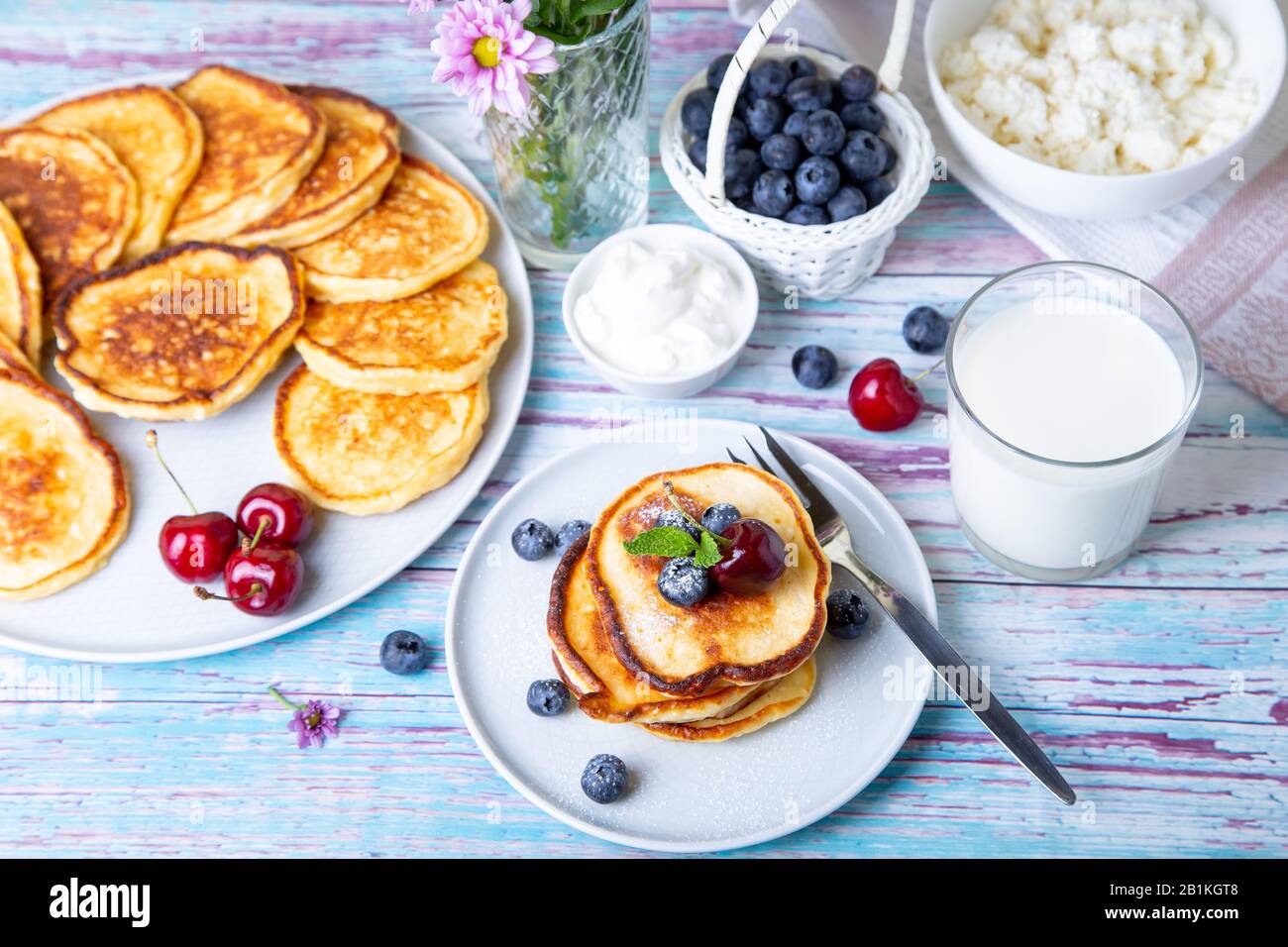 Käsekäse in der Hütte (syrniki). Hausgemachte Käsekuchen aus Hüttenkäse mit Sauerrahm, Beeren und Milch. Traditionelles russisches Gericht. Nahaufnahme. Stockfoto