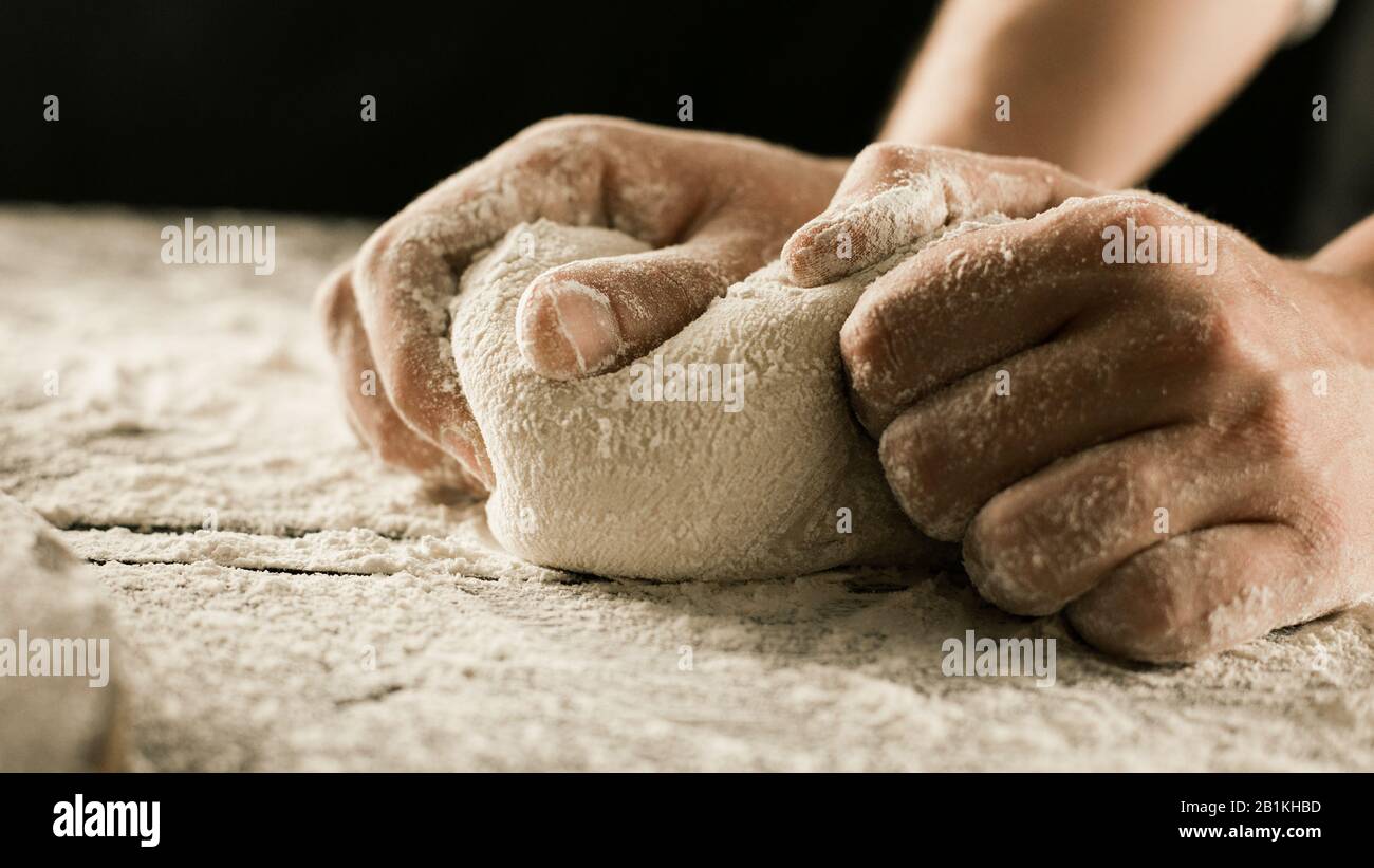 Der Küchenchef übergibt Knetteig mit Mehl auf dem Küchentisch mit seitlichem Blick Stockfoto