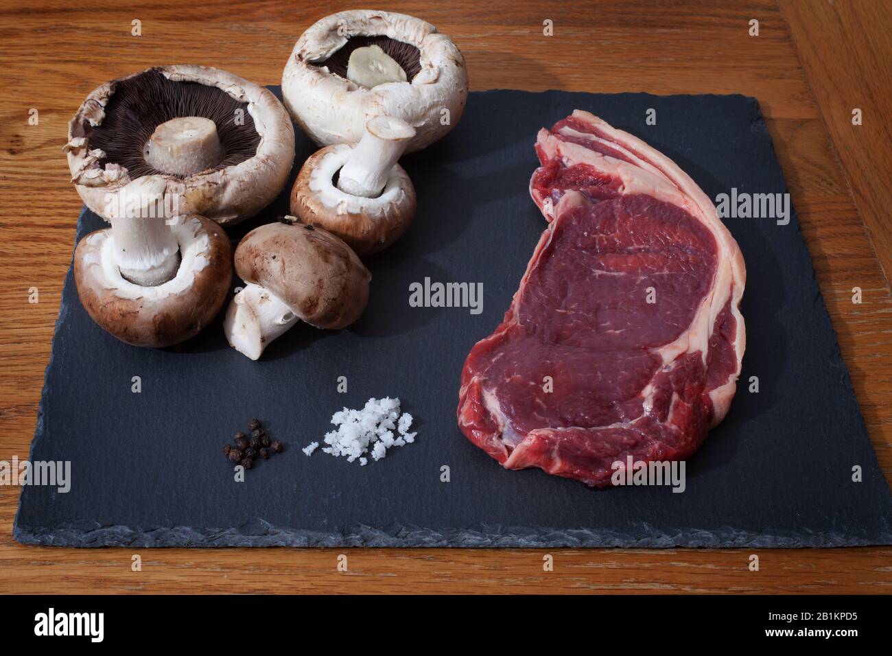 Rohes Rib Eye-Steak, Pilze, Salz und Pfeffer zum Kochen bereit Stockfoto