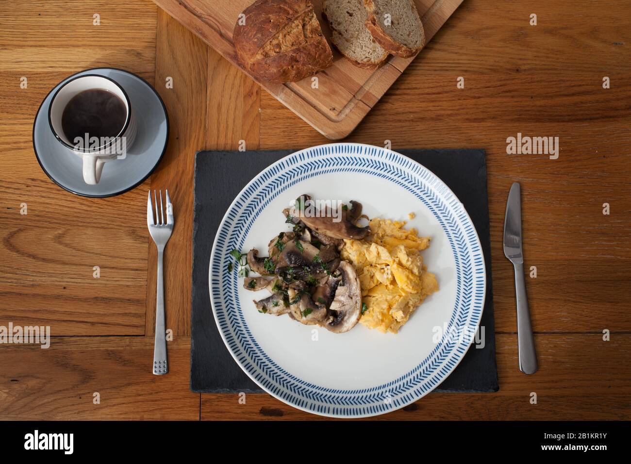 Frühstück mit Rührei, Pilzen, Knoblauch und Koriander, frischem Brot und schwarzem Kaffee Stockfoto