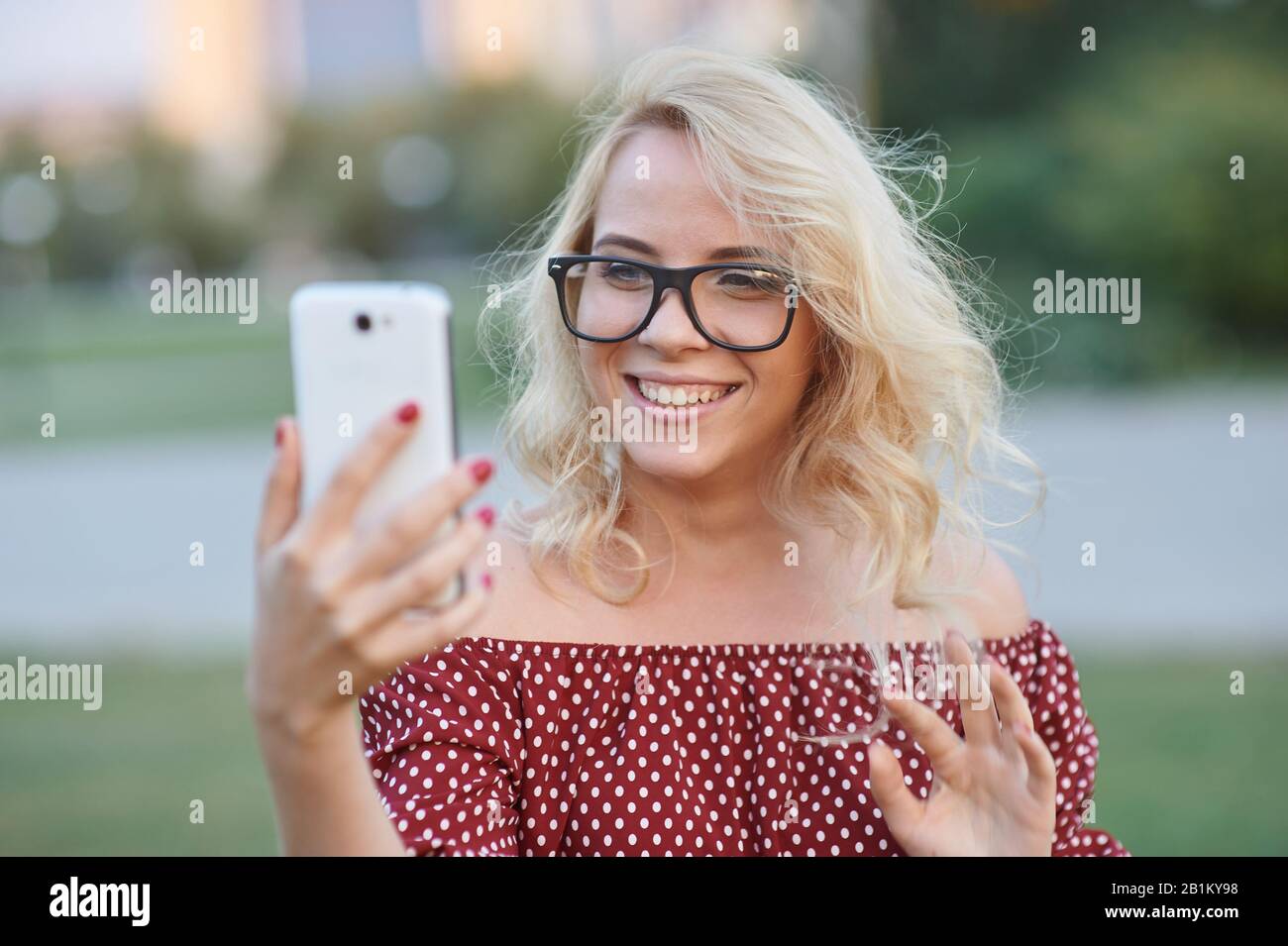Schöne junge Frau Blogger mit blonden Haaren fotografieren auf Smartphone am Straßenhintergrund der Stadt. Hübsches Mädchen mit Smartphone Stockfoto