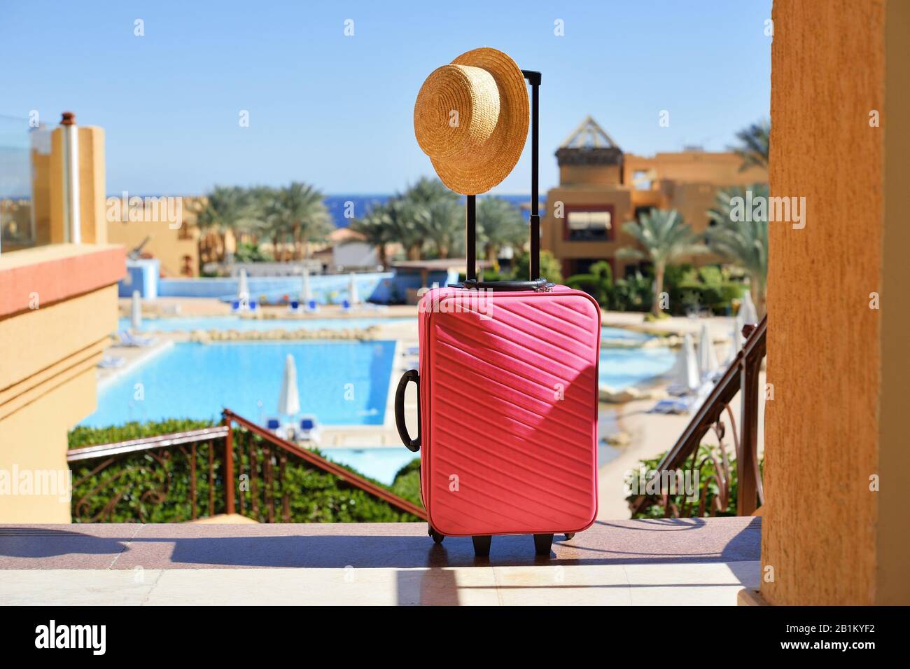 Reise-, Sommerferien- und Urlaubskonzept. Rosafarbener Koffer mit Hut im Hintergrund des Hotelpools in Ägypten Stockfoto Reise-, Sommerferien- und Urlaubskonzept. Rosafarbener Koffer mit Hut im Hintergrund des Hotelpools in Ägypten Stockfoto