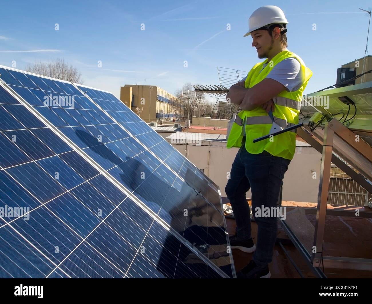 Kaukasisch attraktiver junger Techniker, der die Solarpaneele mit einem Glasreiniger in der Hand betrachtet. Alternative Stromquelle, nachhaltig Stockfoto