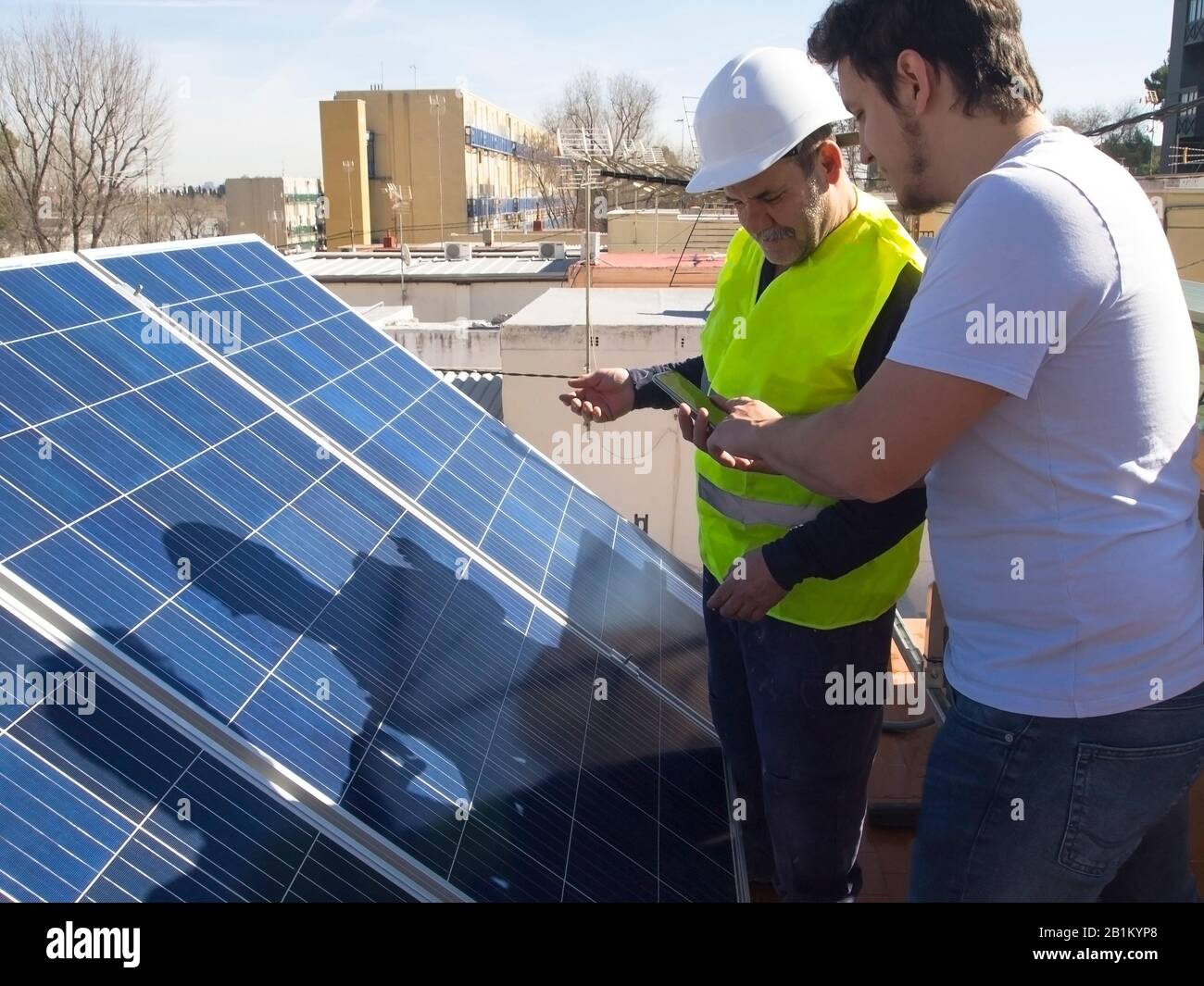 Kaukasischer erfahrener Techniker, der mit seinem jungen Kunden neben den Solarmodulen spricht. Alternative Stromquelle, nachhaltige Ressourcenkonzeption. Stockfoto