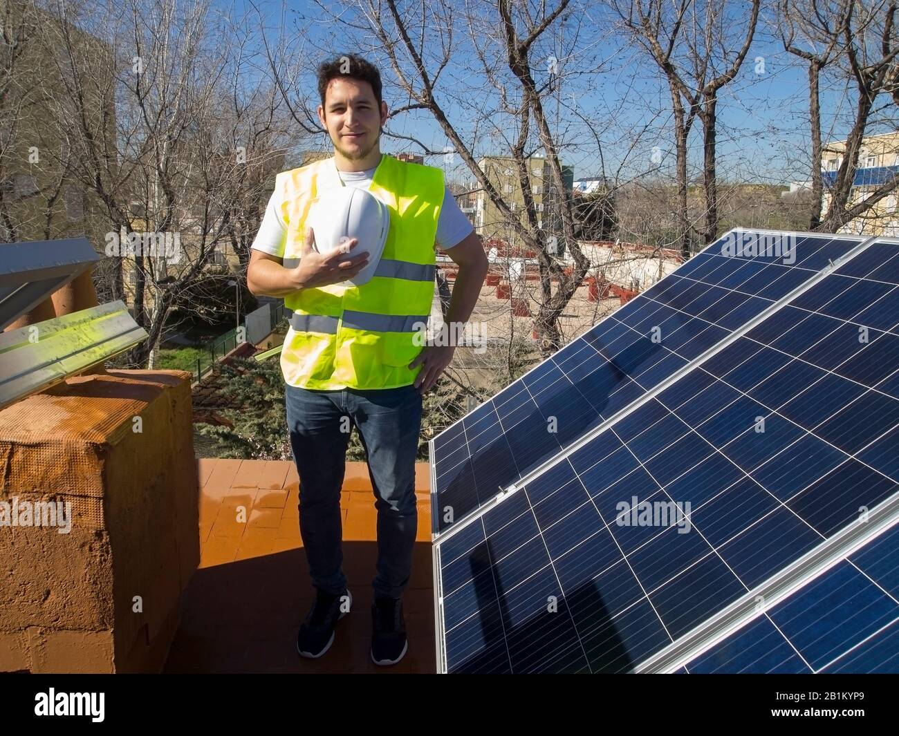 Kaukasisch attraktiver junger Techniker mit Blick auf die Kamera neben den Sonnenkollektoren. Alternative Stromquelle, nachhaltige Ressourcenkonzeption. Stockfoto