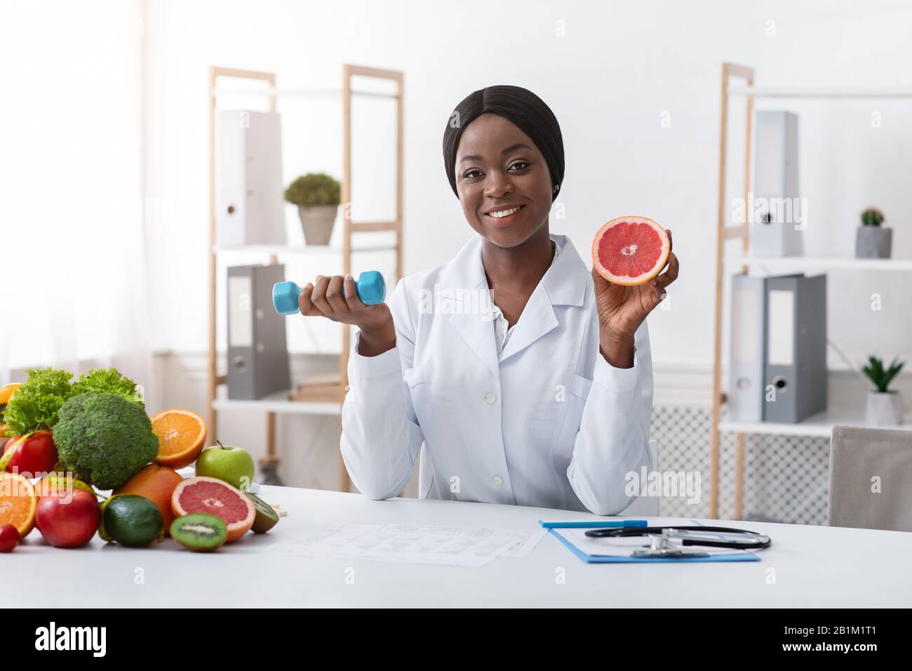 Lächelnder Ernährungsberater, der Grapefruit und Barbell in den Händen hält Stockfoto