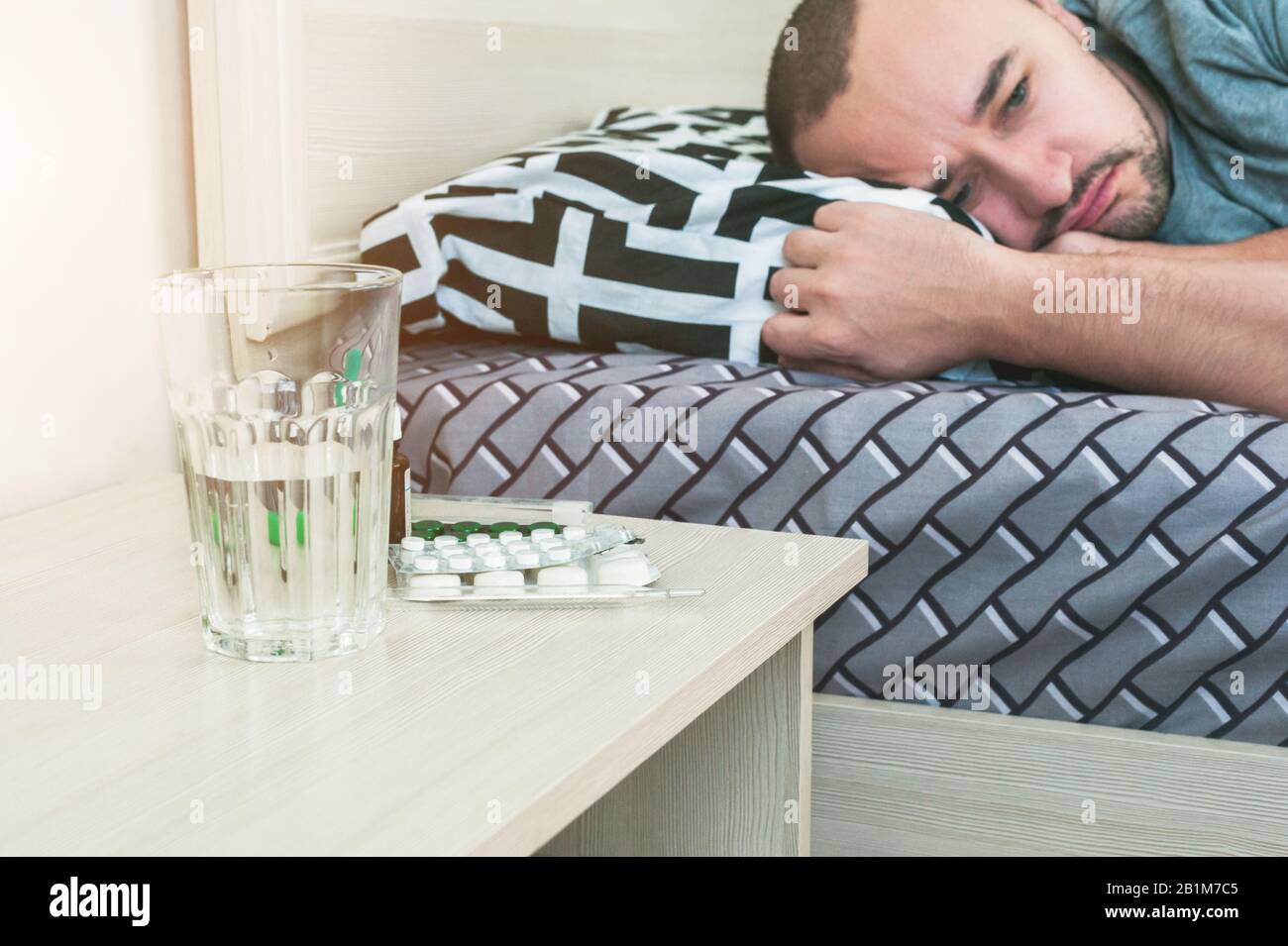 Ein Kranker liegt im Bett, Pillen und Medikamente auf dem Tisch. Stockfoto