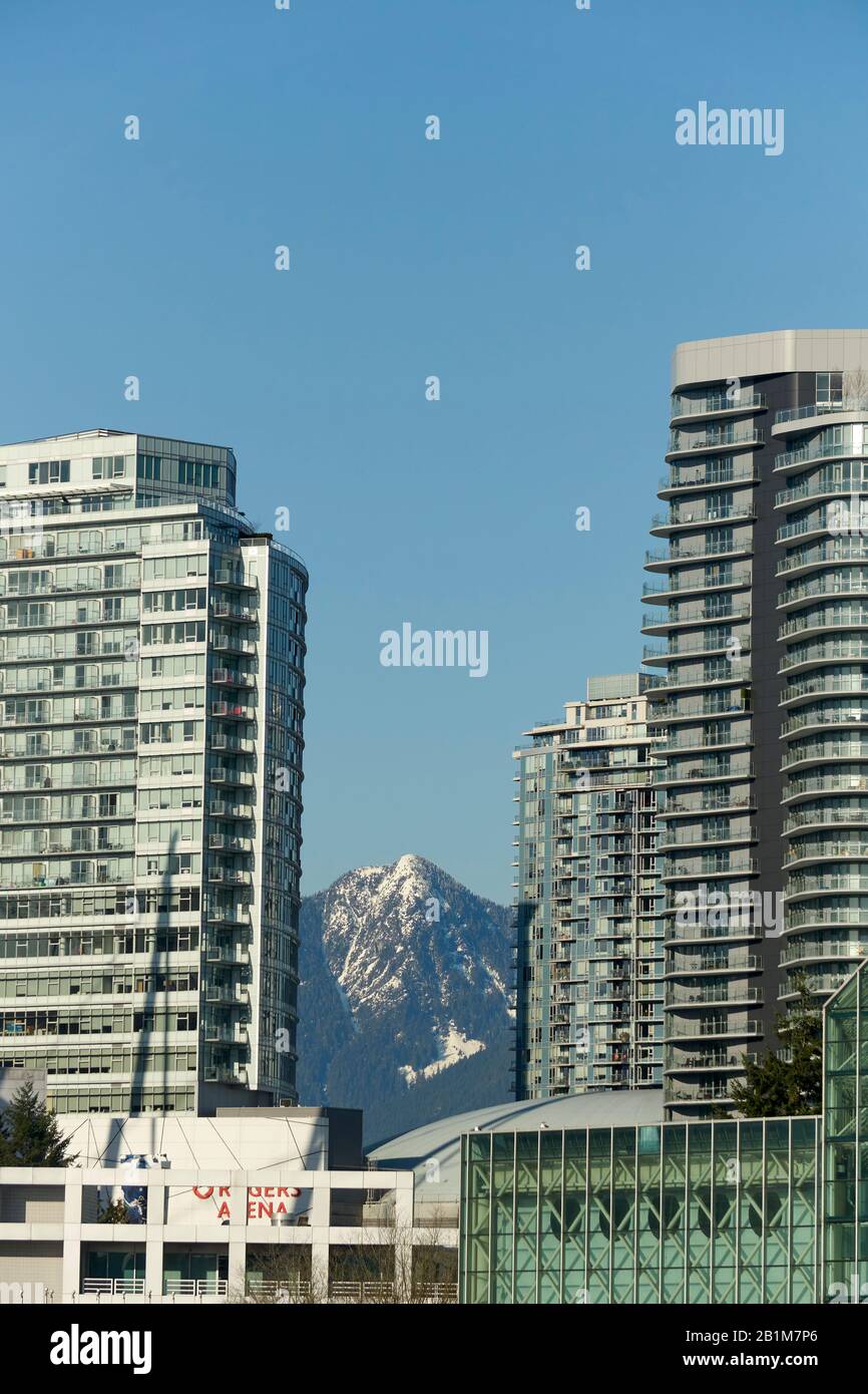 Schneebedeckte Gipfel der North Shore Mountains, die zwischen hohen Wohnhäusern im Stadtzentrum von Vancouver, BC, Kanada, zu sehen sind Stockfoto