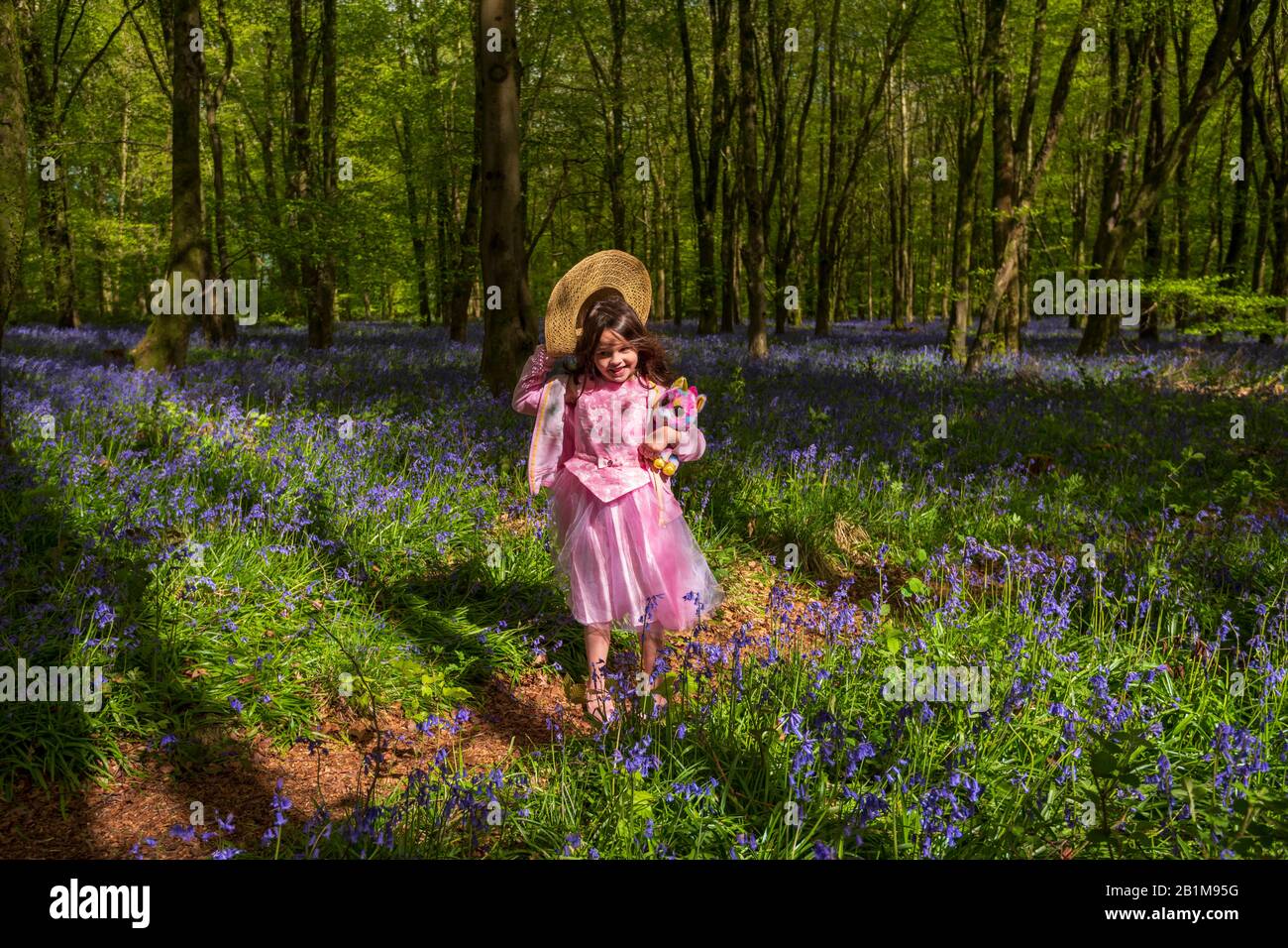 Ein junges Mädchen läuft durch Wald in Dorset mit bläugeln mit Sonne, die durch die buchen- und Birkenüberdachung von leuchtend grünen Blättern glänzen Stockfoto