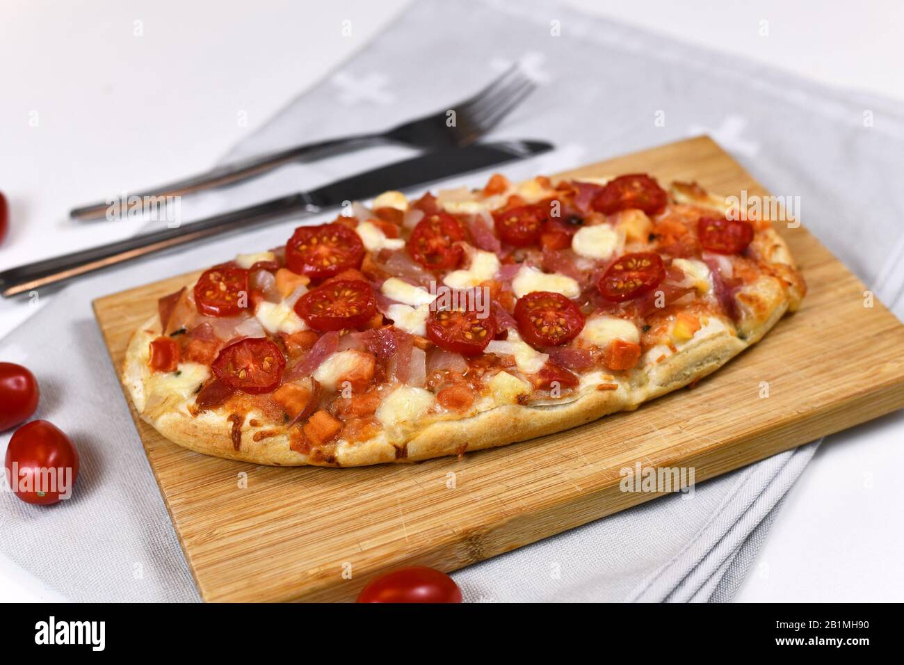 Hausgemachte, ovale Pizza mit Mozzarella-Käse, Tomaten- und Salami-Wurst auf Holzbrett Stockfoto