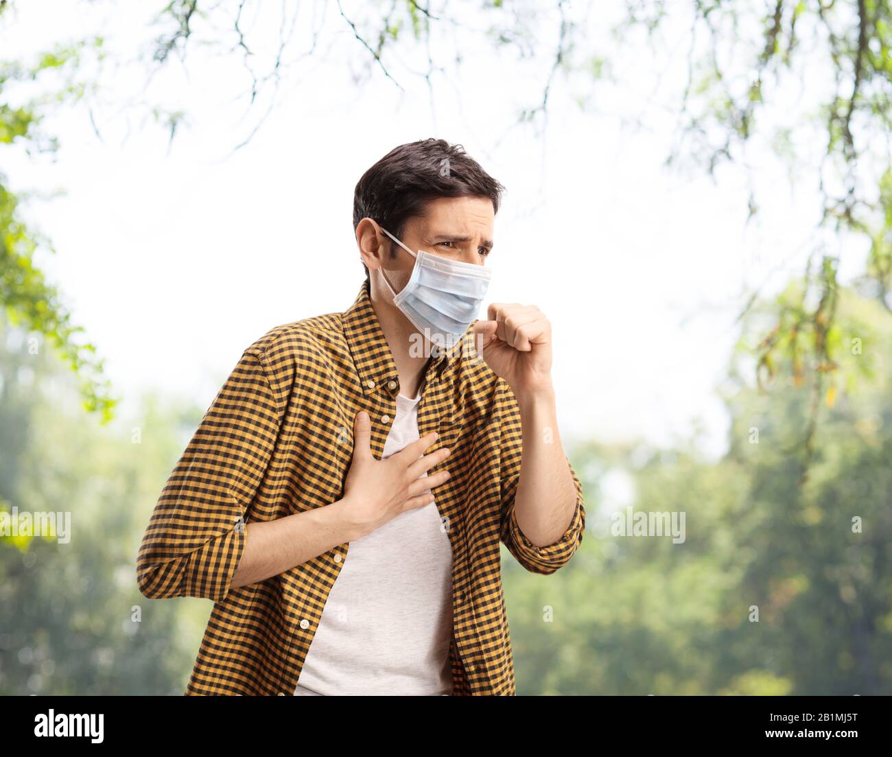 Junger Kerl hustet und trägt eine Gesichtsmaske im Freien in einem Park Stockfoto