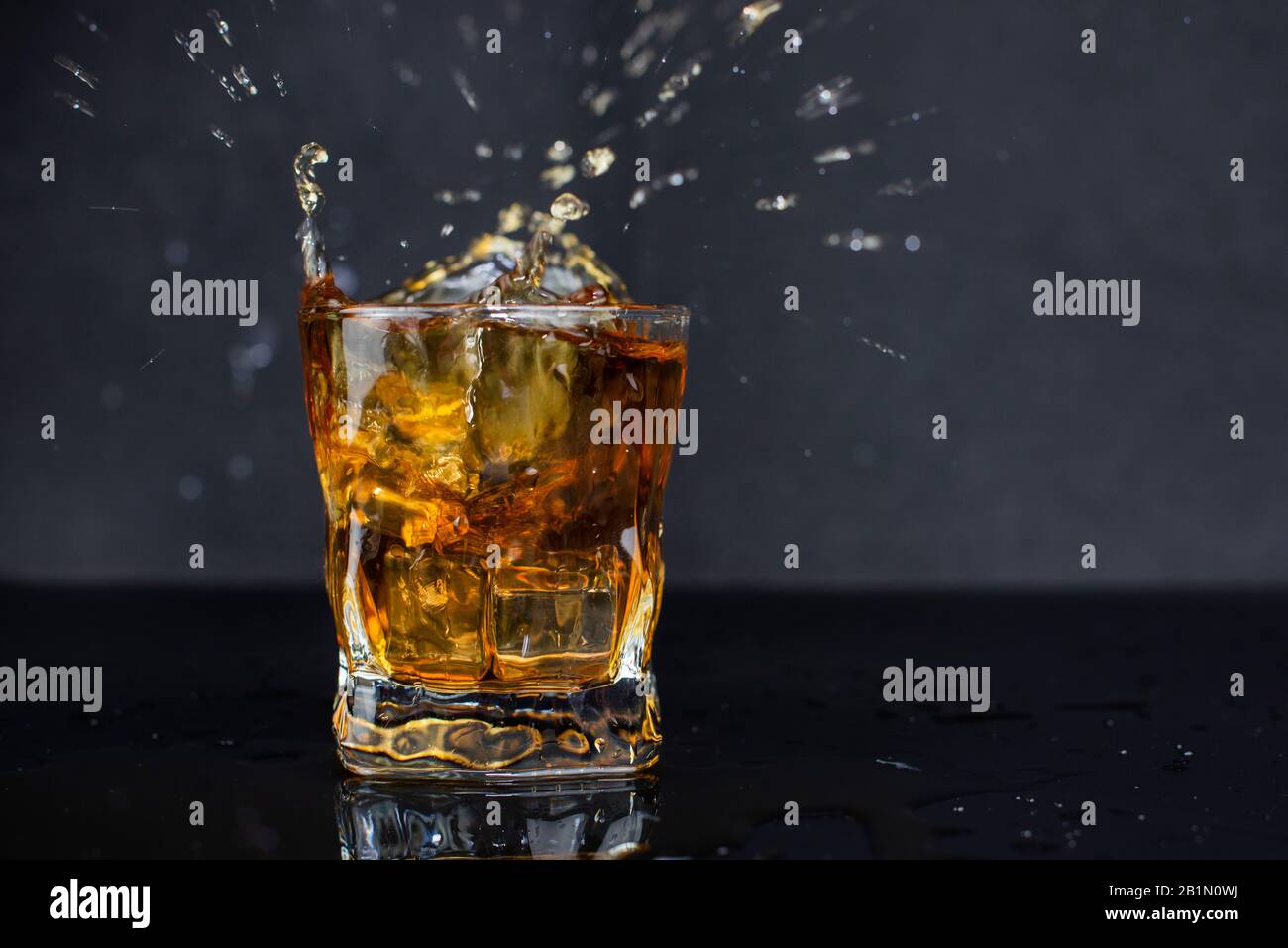 Spritzer Alkohol trinken Whiskey mit Eis mit Tropfen in einem Glas auf schwarzem Hintergrund Stockfoto