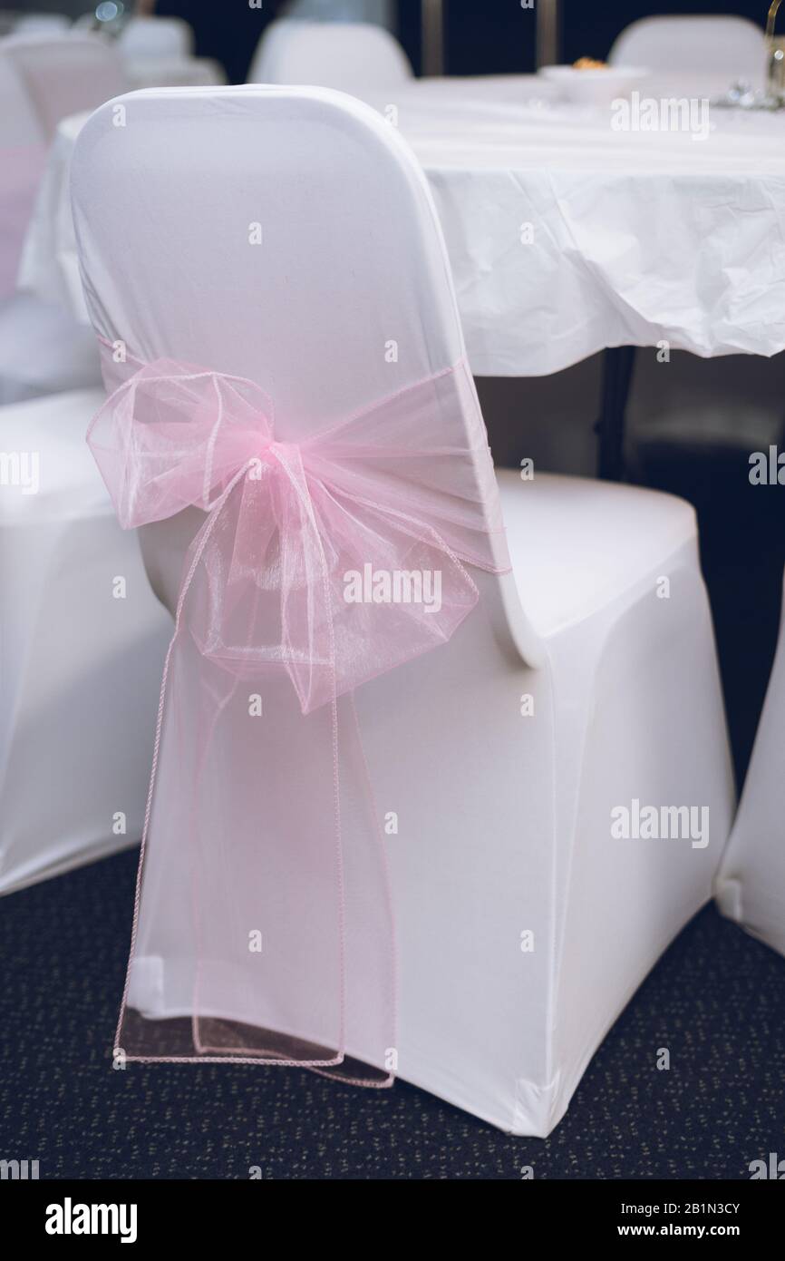 Rosafarbene Bögen, die um Stühle mit weißen Abdeckungen für Hochzeitsdekorationen gebunden sind Stockfoto