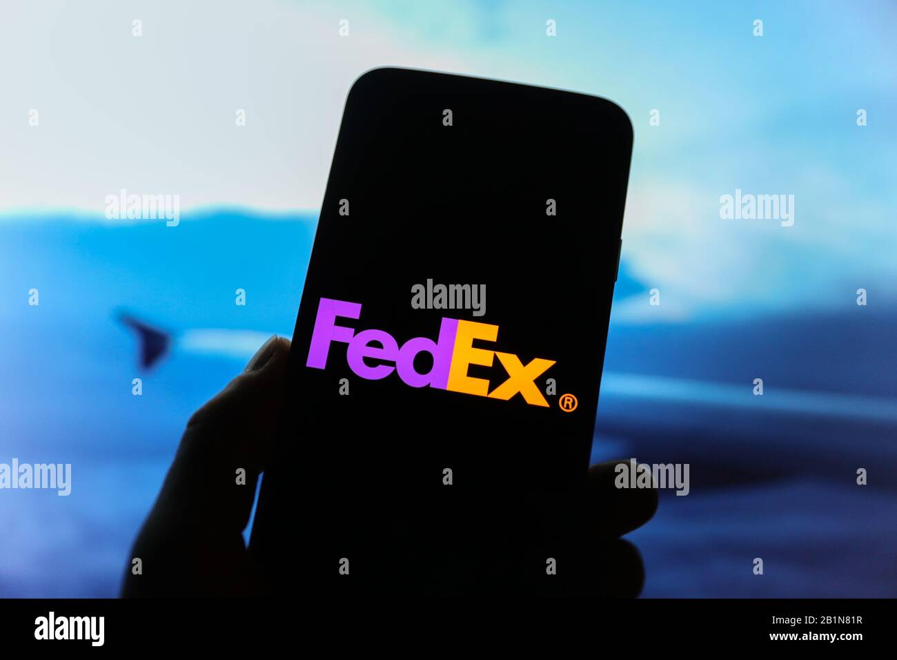FedEx Firmenlogo auf dem Smartphone-Bildschirm mit Blick aus dem Flugzeug und einem Flugzeugflügel, der im Hintergrund verschwommen zu sehen ist Stockfoto