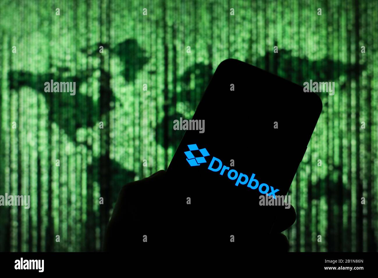 Dropbox Online-Cloud-Firmenlogo wird auf dem Smartphone-Bildschirm mit einer Matrix-ähnlichen Weltkarte angezeigt, die im Hintergrund verschwommen zu sehen ist Stockfoto