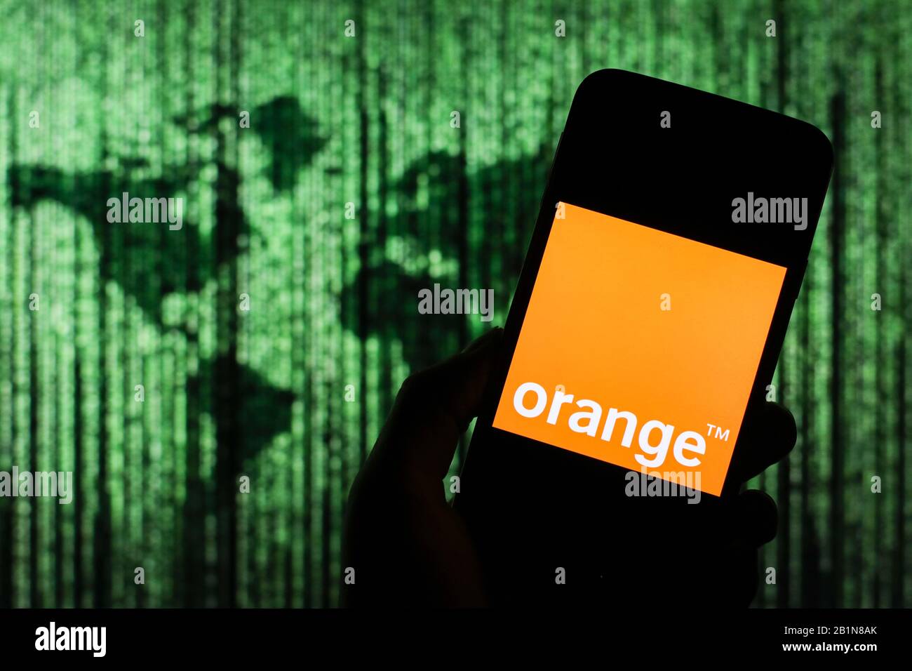 Orangefarbenes Firmenlogo für Telekommunikationsunternehmen, das auf dem Smartphone-Bildschirm angezeigt wird, mit einer Matrix-ähnlichen Weltkarte, die im Hintergrund verschwommen zu sehen ist Stockfoto
