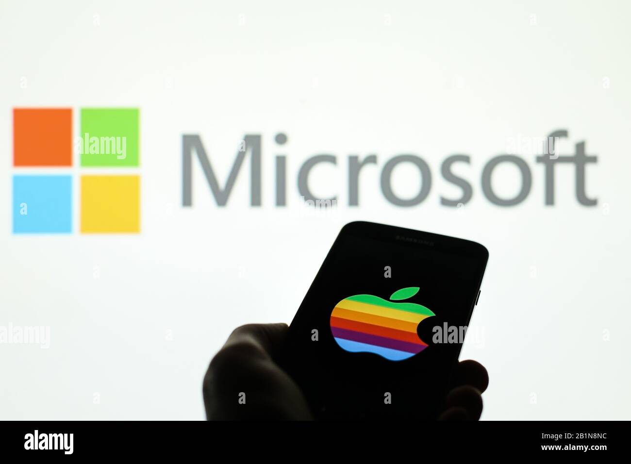 Das Apple Firmenlogo wird auf dem Smartphone-Bildschirm angezeigt, wobei das Microsoft-Logo im Hintergrund verschwommen zu sehen ist Stockfoto