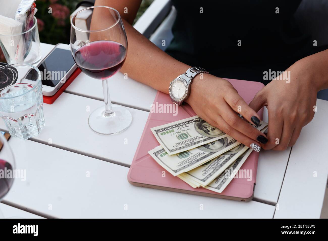 Geldscheine Dollar in die Hände eines Mädchens Geschäftsmann für den Kauf einer Zahlung, die in einem Restaurant an einem Tisch mit einer plaghet und einem Glas Wein sitzt Stockfoto