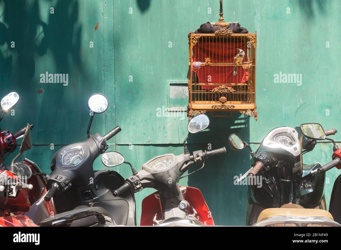 Saigon (Ho-Chi-Minh-Stadt) Vogelkäfig - EIN Vogelkäfig, der unter geparkten Motorrädern in Saigon, Vietnam, Südost-Asien hängt. Stockfoto