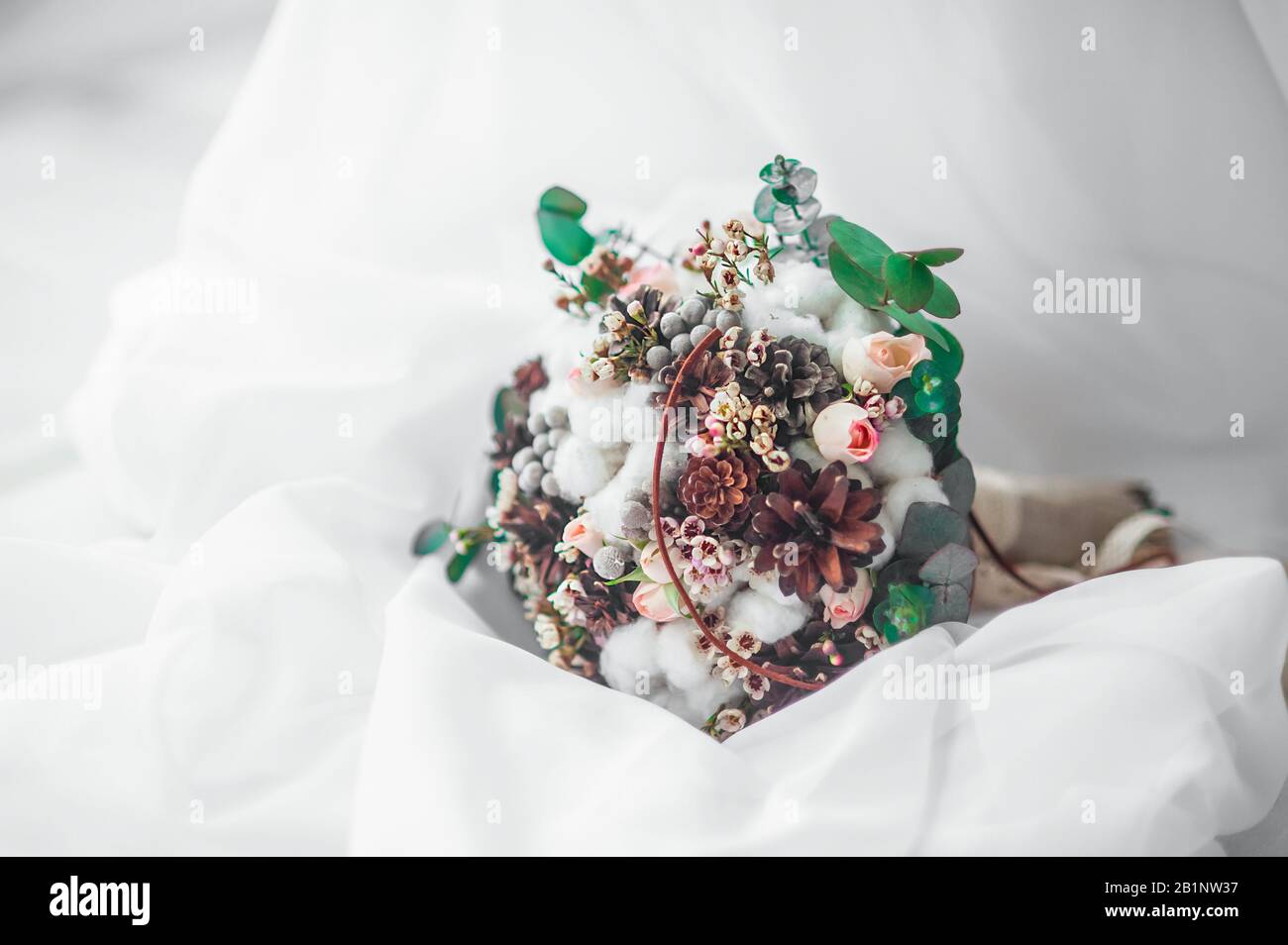 Stilvoller winter-brautstrauß aus zarten rosafarbenen Rosen, Baumwollblüten und Eukalyptusblättern und Pflanzen in einem weißen Tüllengewebe Stockfoto