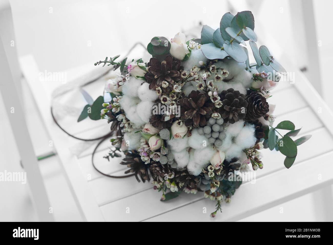 Stilvoller winter-brautstrauß aus zarten rosafarbenen Rosen, Baumwollblüten und Eukalyptusblättern und Pflanzen auf weißem Holz Stockfoto