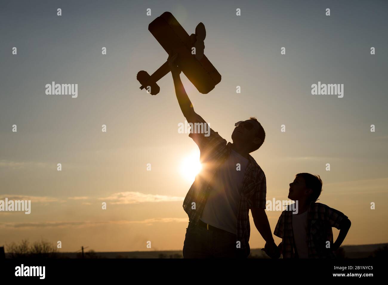 Vater und Sohn spielen mit Pappe Spielzeugflugzeug im Park bei Sonnenuntergang. Konzept der freundlichen Familie. Leute, die Spaß im Freien. Stockfoto