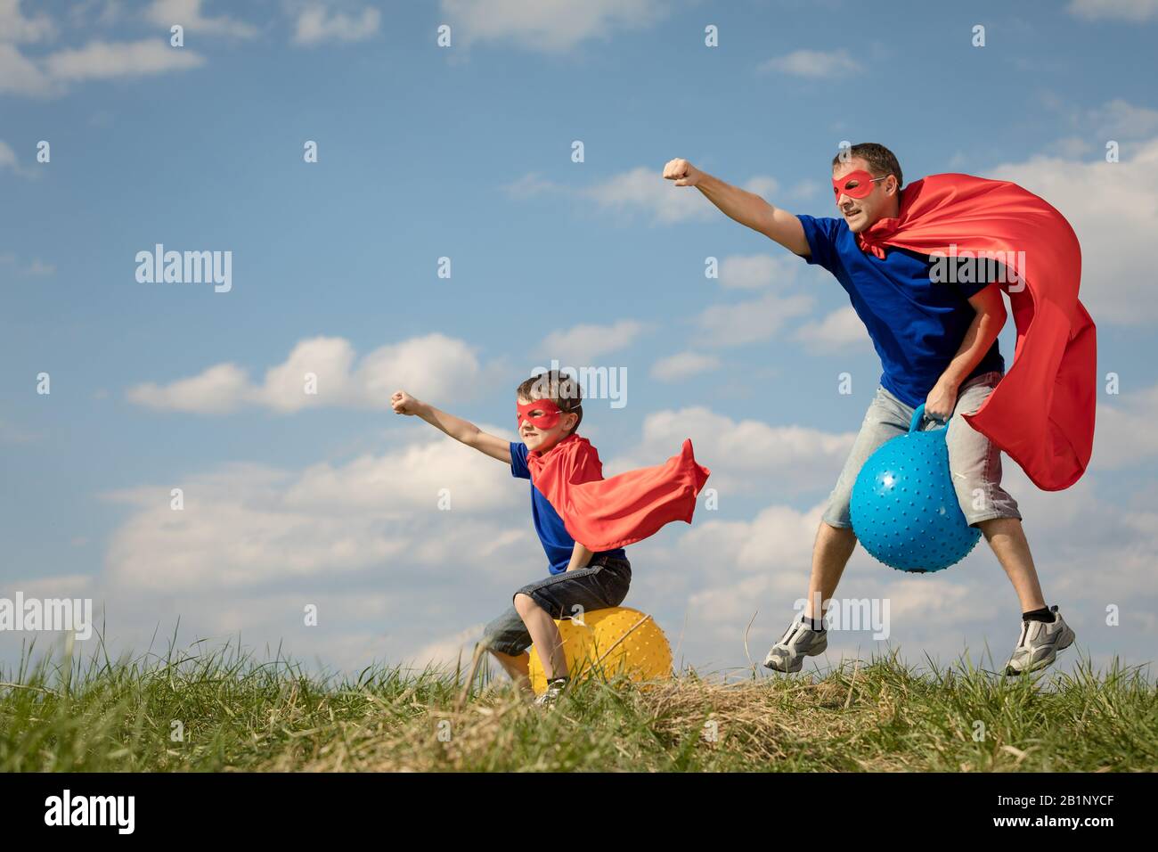 Vater und Sohn spielen Superhelden in der Tageszeit. Leute, die Spaß im Freien. Sie springen auf aufblasbaren Bällen auf dem Rasen. Konzept der freundlichen Familie. Stockfoto