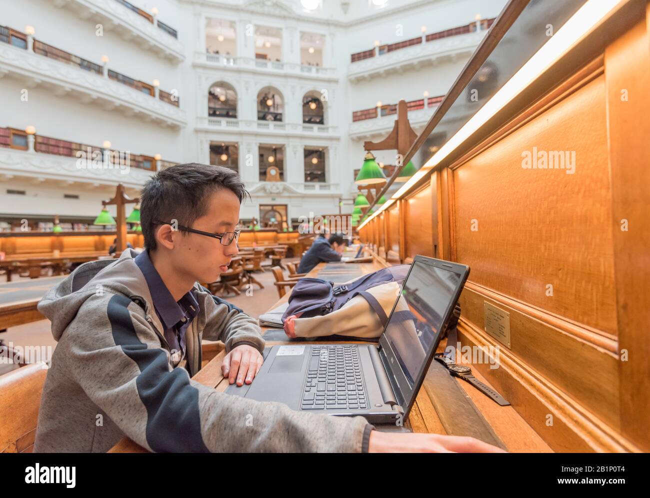 An einem der historischen Radiationsschalter im La Trobe Reading Room der State Library of Victoria sitzt ein junger asiatischer Junge, der von einem Laptop liest Stockfoto