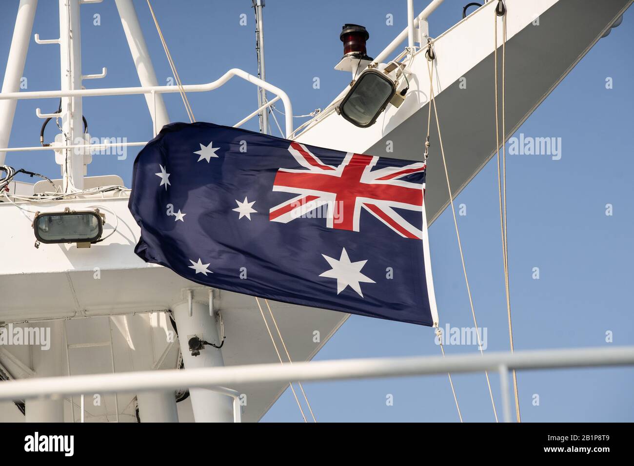 Rot-weiße und blaue australische Flagge, die an einem blauen Tag bei starkem Wind auf einem Kreuzfahrtschiffmast fliegt Stockfoto
